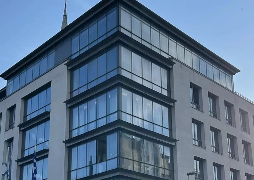 Eine Wissenschaftlerin und ein Wissenschaftler arbeiten hinter einer Glasfassade und mischen Chemikalien mit Großgeräten.