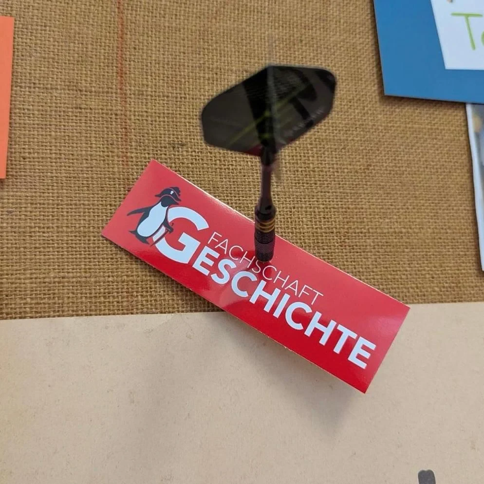 Eine Wissenschaftlerin und ein Wissenschaftler arbeiten hinter einer Glasfassade und mischen Chemikalien mit Großgeräten.