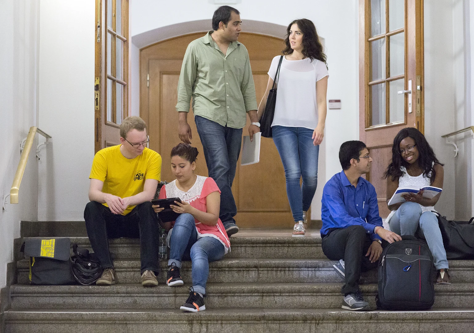 Eine Wissenschaftlerin und ein Wissenschaftler arbeiten hinter einer Glasfassade und mischen Chemikalien mit Großgeräten.