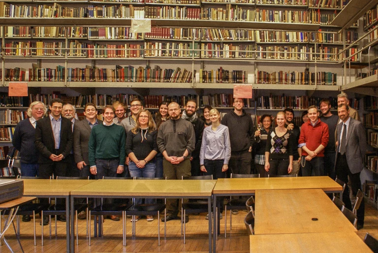 Eine Wissenschaftlerin und ein Wissenschaftler arbeiten hinter einer Glasfassade und mischen Chemikalien mit Großgeräten.