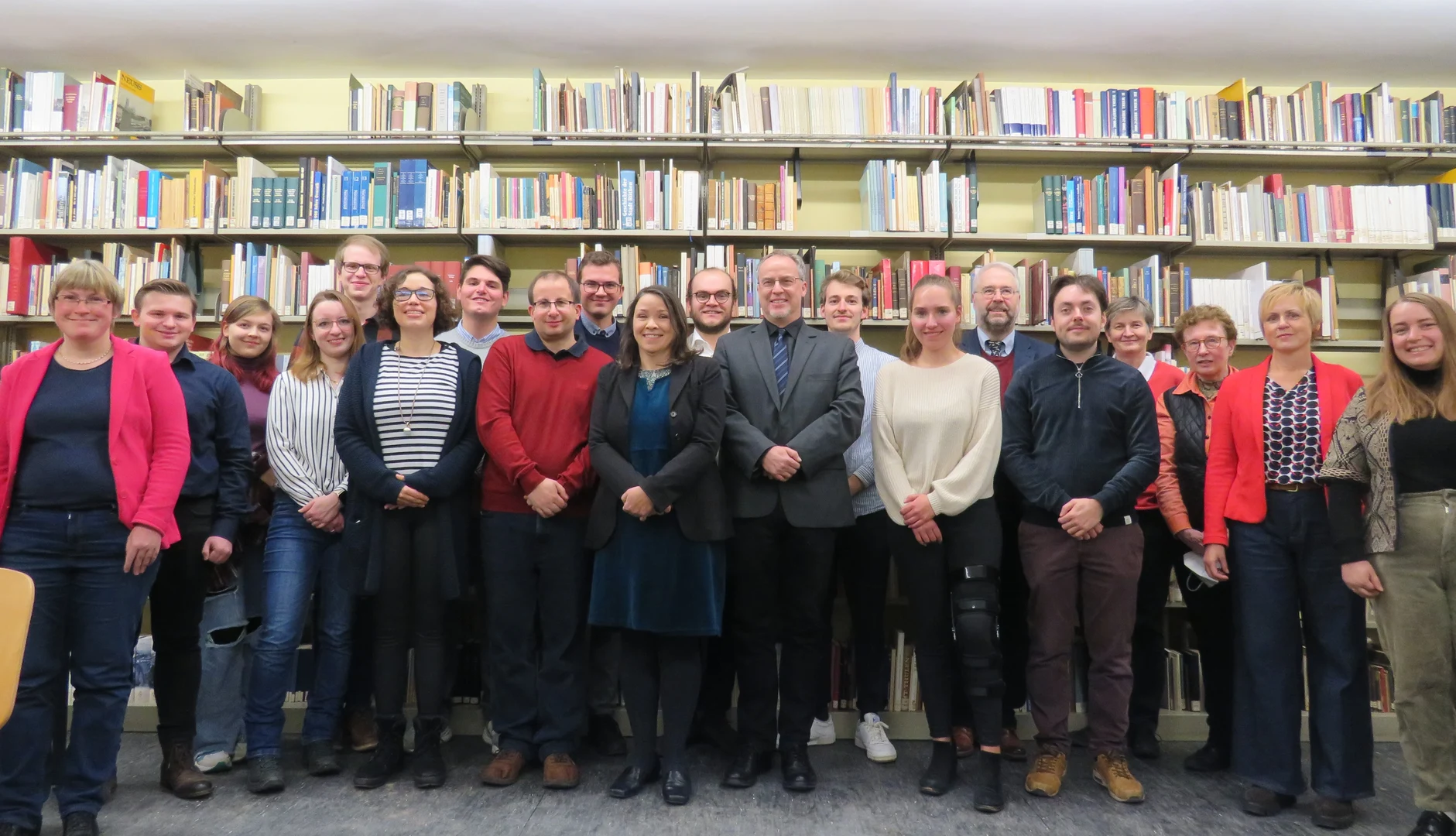 Eine Wissenschaftlerin und ein Wissenschaftler arbeiten hinter einer Glasfassade und mischen Chemikalien mit Großgeräten.