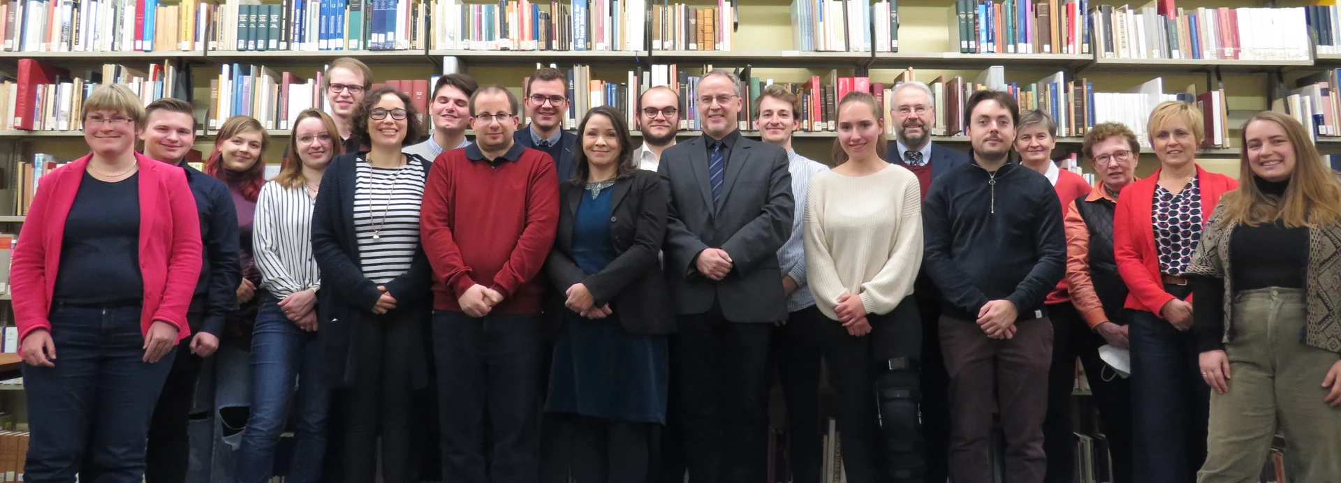 Eine Wissenschaftlerin und ein Wissenschaftler arbeiten hinter einer Glasfassade und mischen Chemikalien mit Großgeräten.