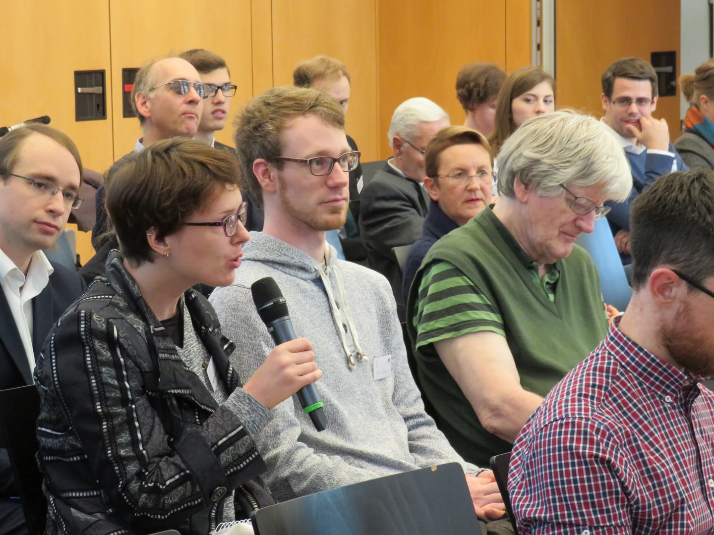 Eine Wissenschaftlerin und ein Wissenschaftler arbeiten hinter einer Glasfassade und mischen Chemikalien mit Großgeräten.