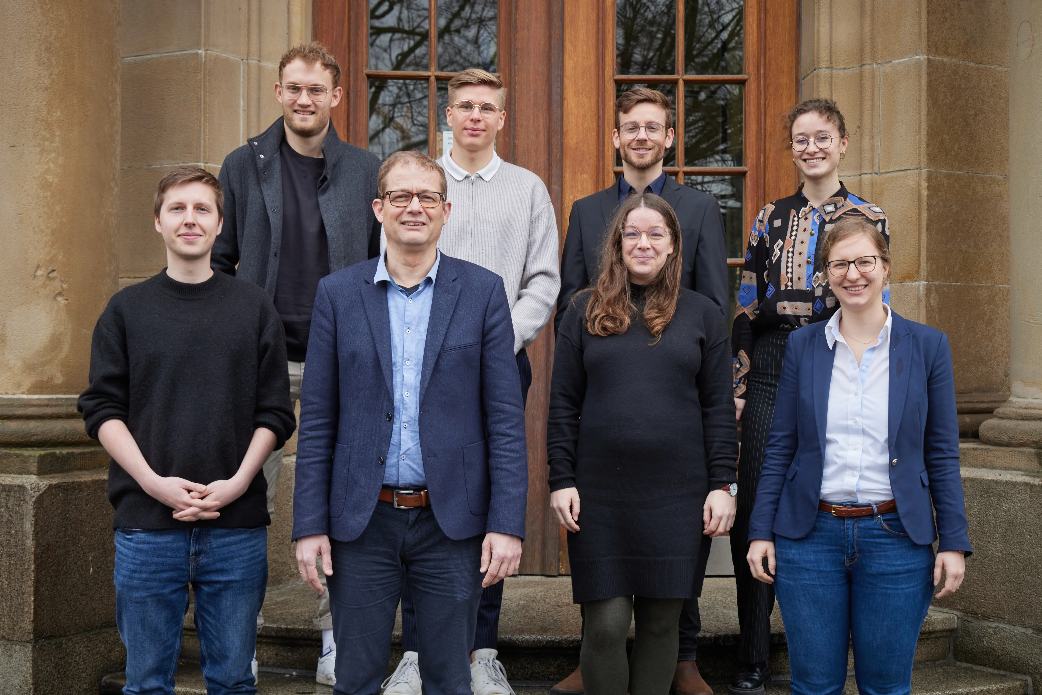 Eine Wissenschaftlerin und ein Wissenschaftler arbeiten hinter einer Glasfassade und mischen Chemikalien mit Großgeräten.