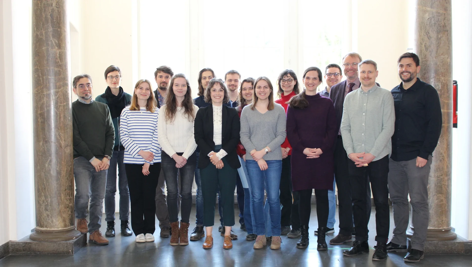 Eine Wissenschaftlerin und ein Wissenschaftler arbeiten hinter einer Glasfassade und mischen Chemikalien mit Großgeräten.