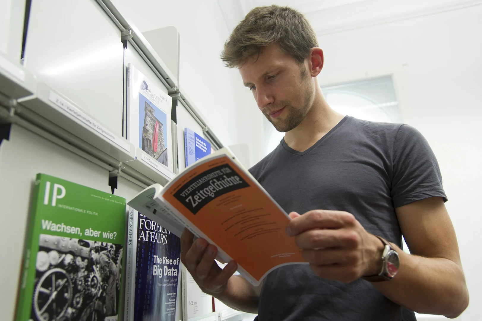 Eine Wissenschaftlerin und ein Wissenschaftler arbeiten hinter einer Glasfassade und mischen Chemikalien mit Großgeräten.